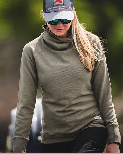 Person wearing a green long-sleeve shirt and cap with sunglasses, outdoors.