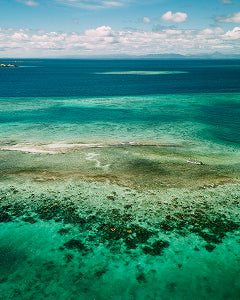 Clear turquoise ocean waters with a small island in the distance under a blue sky.