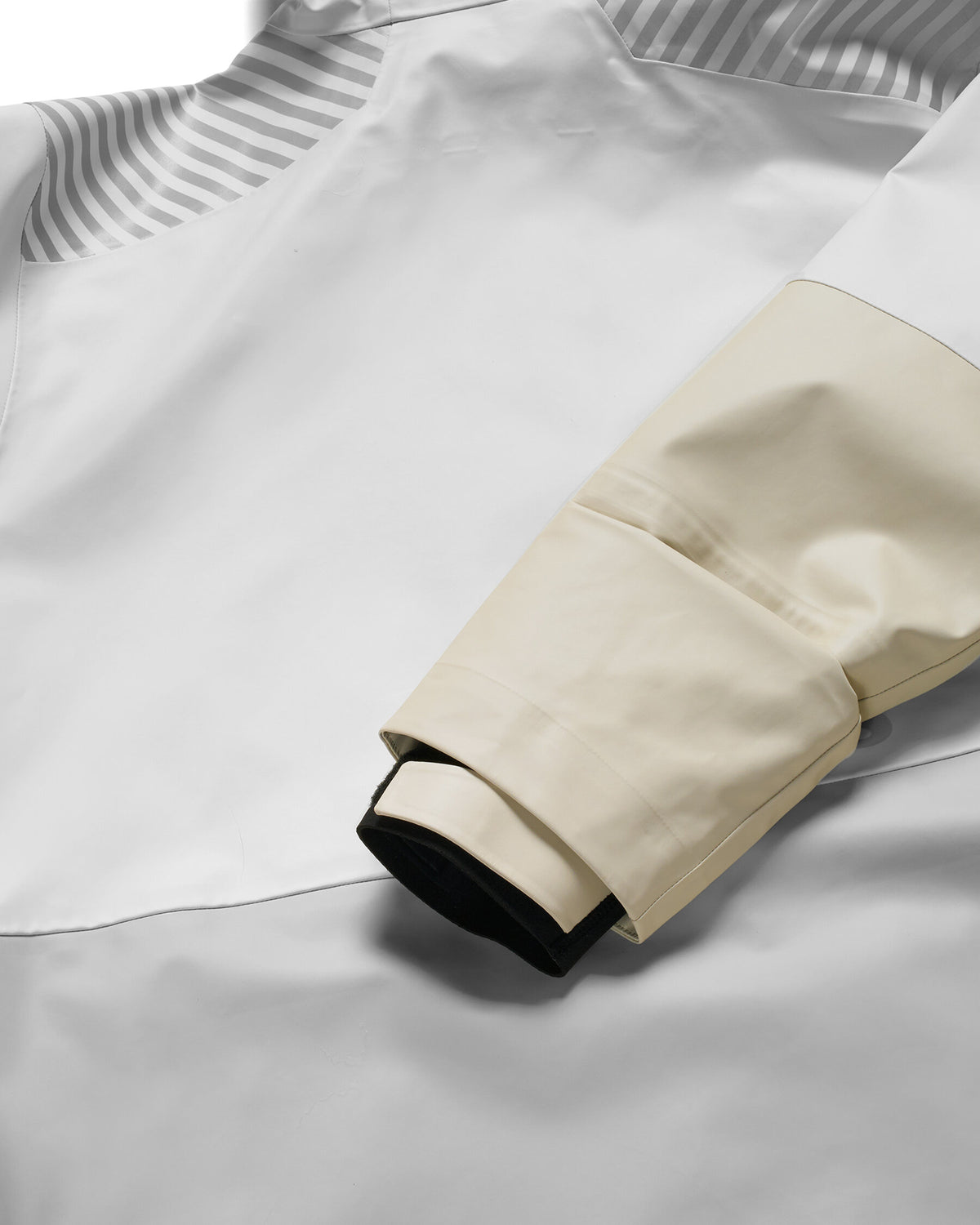 Close-up detail of a white jacket or coat sleeve with a cream-colored cuff overlay and a black inner lining, set against a matching white fabric background. Alabaster
