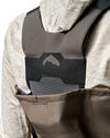 Women's Waders G3 Pro Guide Stockingfoot Close-up of a person wearing gray and black waterproof waders over a light beige patterned hooded jacket, with a fish logo visible on the chest.