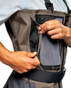 Men's G3 Pro Bootfoot Waders Close-up of a person wearing a gray and black Simms fishing wader, demonstrating the zippered pocket on the front.