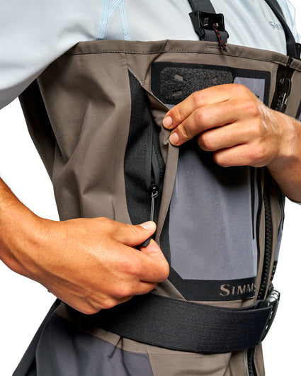 Men's G3 Pro Bootfoot Waders Close-up of a person wearing a gray and black Simms fishing wader, demonstrating the zippered pocket on the front.