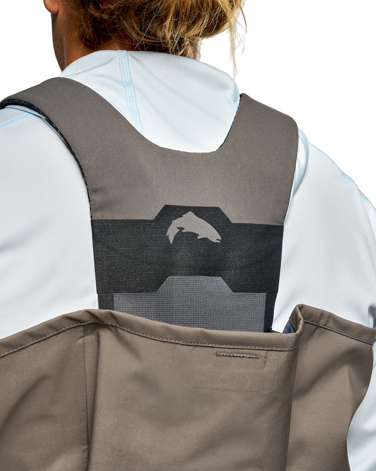 Men's G3 Pro Bootfoot Waders Close-up back view of a person wearing a gray and black back support harness vest over a white and light blue athletic jacket, with a taupe waterproof shell attached.