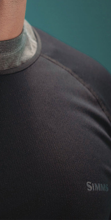 Close-up of a person wearing a black garment with 'Simms' branding on a teal background