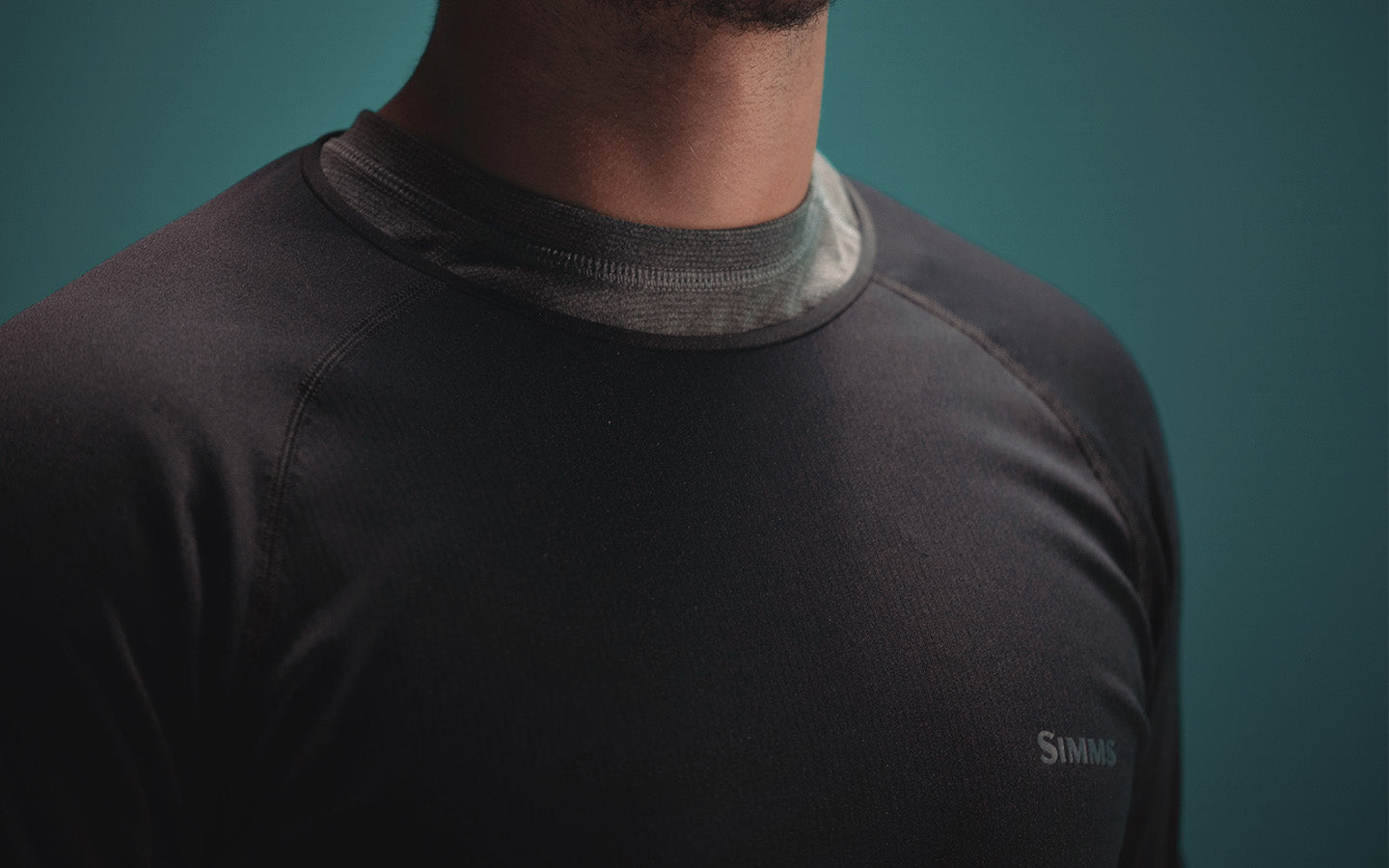 Person wearing a black shirt with a visible brand logo against a teal background