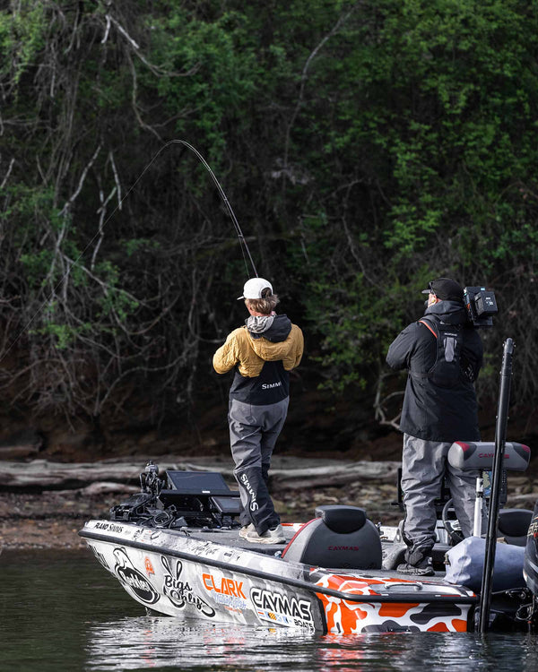 Two people on a boat fishing in a forested area